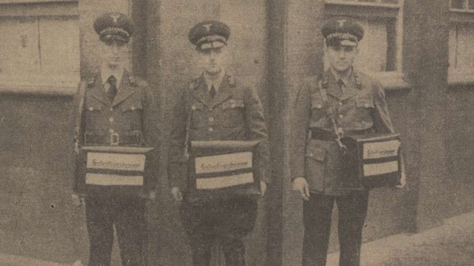 Drei Zeitungsverkäufer in Uniform, die den Hakenkreuzbanner anbieten.