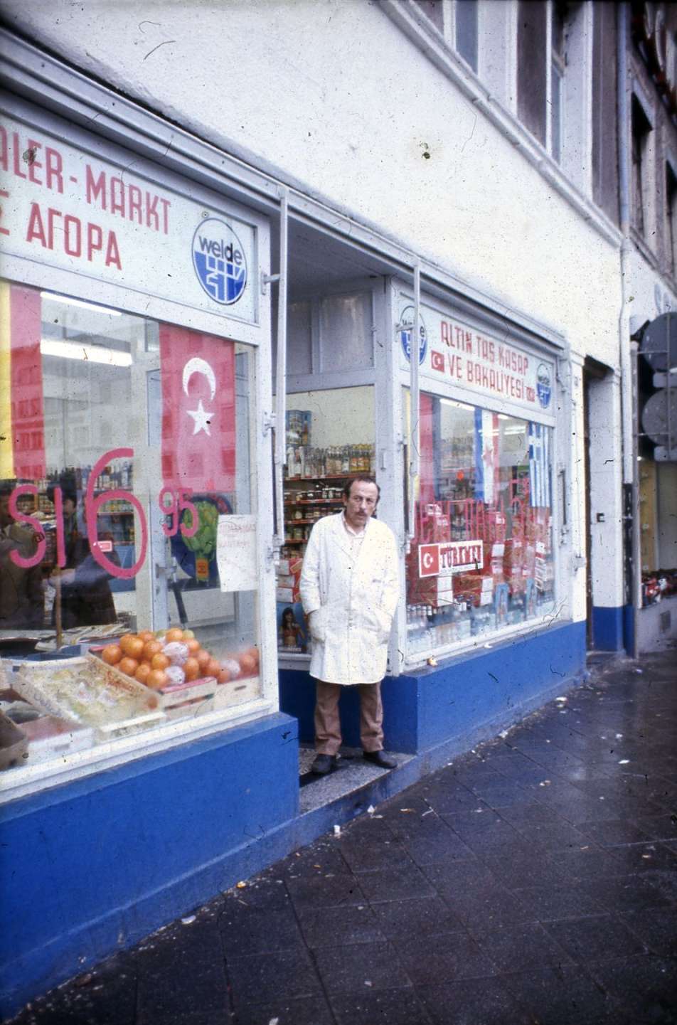 farbiges Foto eins türkischen Gastarbeiters, der an einem Geschäft steht, 1960er Jahre