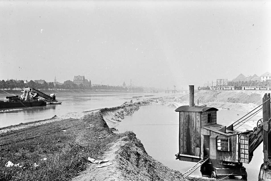 Schwarz-Weiß-Fotografie vom Fluss Neckar mit Uferpromenade auf der linken Seite und einer Baugrube mit Bagger auf der rechten Seite