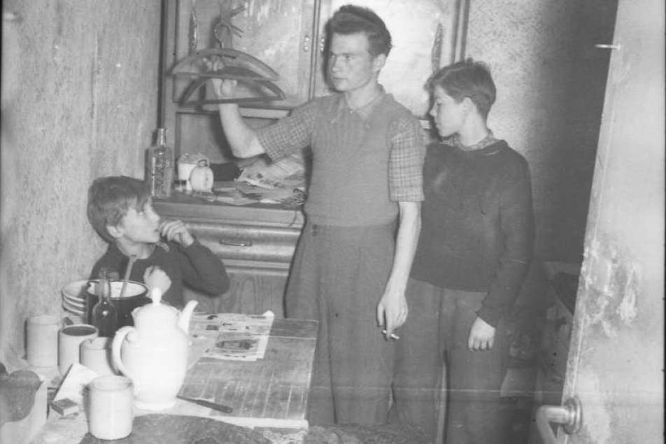 Fotografie in schwarz-weiß zeigt drei junge Menschen in einem Innenraum eines Bunkers mit Mobiliar 