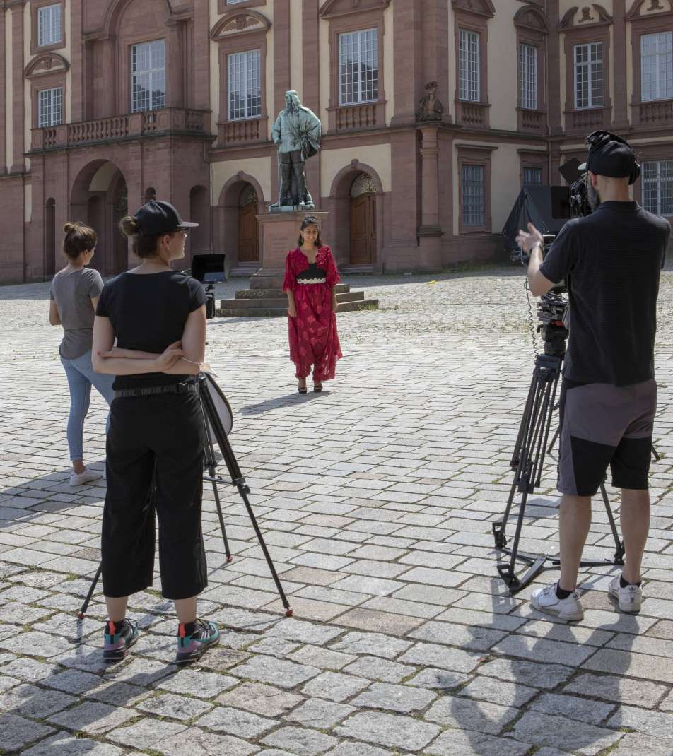 Drei Menschen mit Kamera-Ausrüstung vor einer Person in roter Kleidung vor dem Mannheimer Schloss