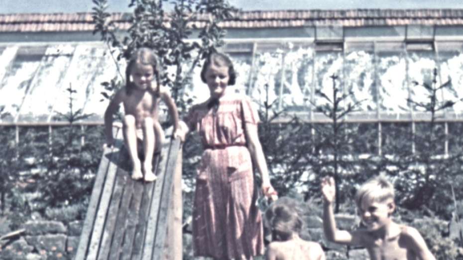 Die Mutter Hedwig Höß steht mit ihren Kindern in einem Garten an einer Wasserrutsche. Der Garten ist die Villa Höß im KZ Auschwitz