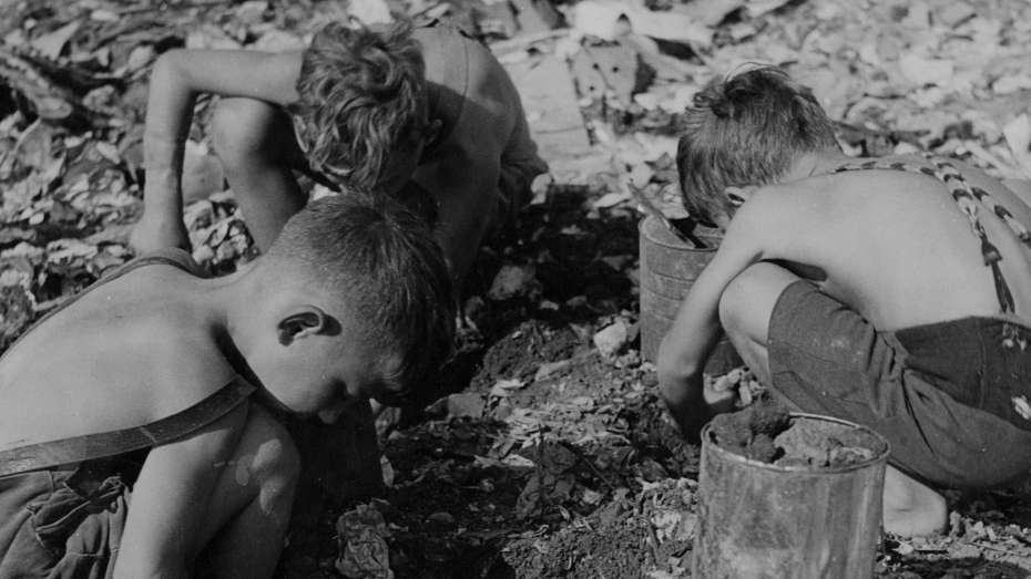 schwarz-weiß Fotografie von drei Kindern, die auf dem Boden knien und nach Kohleresten suchen, 1949