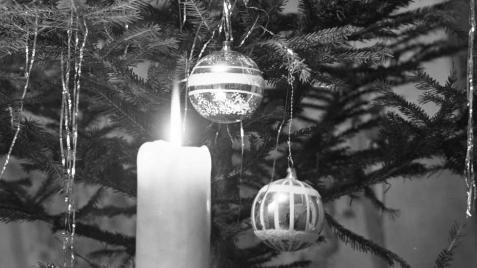 schwarz-weiß Foto von Schmuck am Weihnachtsbaum, das eine brennende Kerze, Kugeln und Lametta zeigt