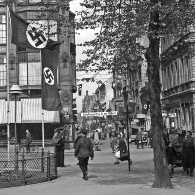 Beflaggung anlässlich der Wahl zum "Anschluss" Österreichs in den Quadraten P 1 u. P 2. Es laufen Menschen unter Hakenkreuzfahnen, die an den Wänden hängen.
