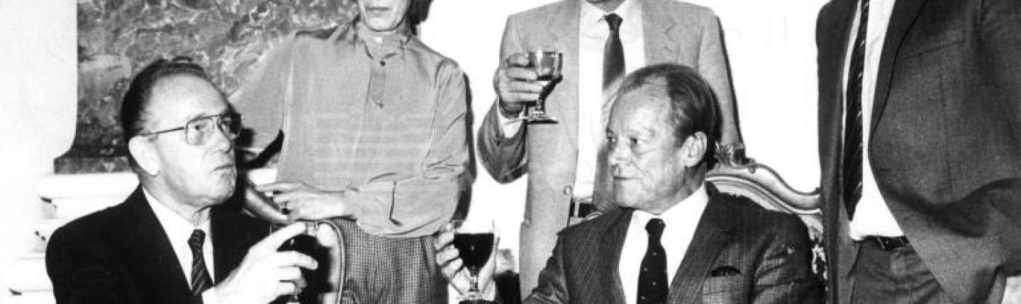 Zwei Männer gehobenen Alters sitzen vor einer Frau und zwei Männern im gleichen Alter. Die Herrschaften haben Getränke in der Hand. Sie sind von links: DGB-Vorsitzender Heinz-Oskar Vetter (1917-1990), SPD-Vorsitzender Willy Brandt (1913-1992); stehend von links: Maria Braun (DGB Mannheim), Fritz Karg, Erster Bürgermeister Manfred David (SPD)