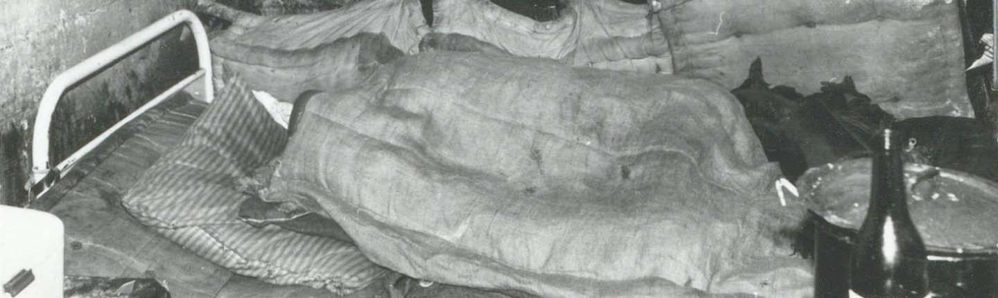 schwarz-weiß Foto einer Bunkerzelle mit einem ungemachten Bett im Hintergrund, 1964