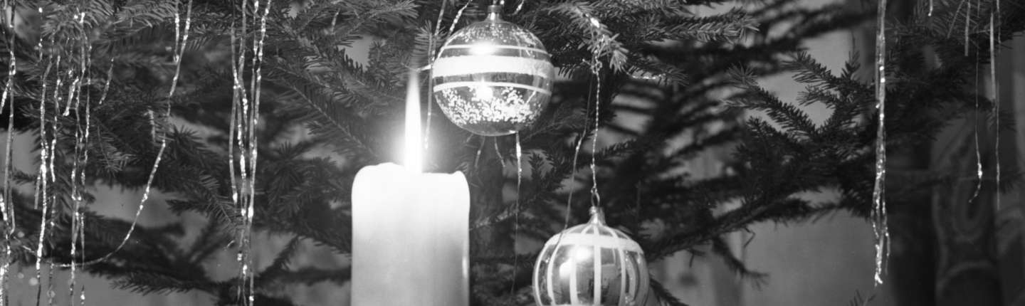 schwarz-weiß Foto von Schmuck am Weihnachtsbaum, das eine brennende Kerze, Kugeln und Lametta zeigt