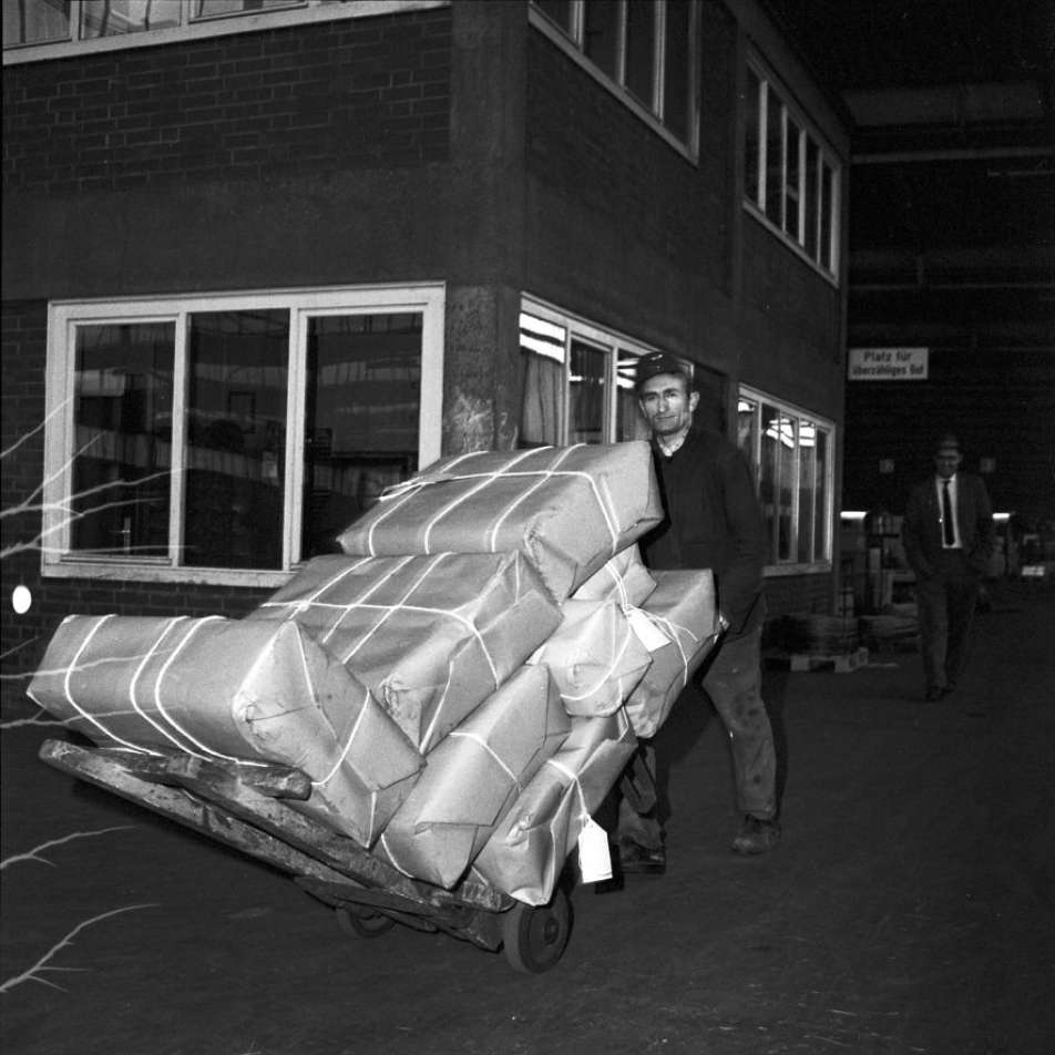 schwarz-weiß Fotografie eines Gastarbeiters, der Pakete auf einer Sackkarre trägt