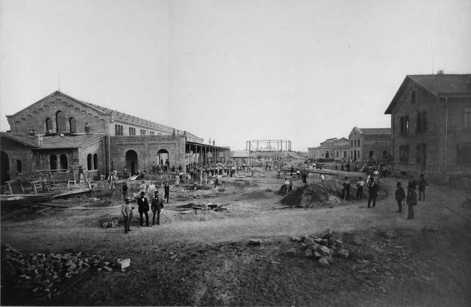 Fotografie in schwarz-weiß von einem Fabrikgelände mit Arbeitern auf dem Areal zwischen den Fabrikgebäuden