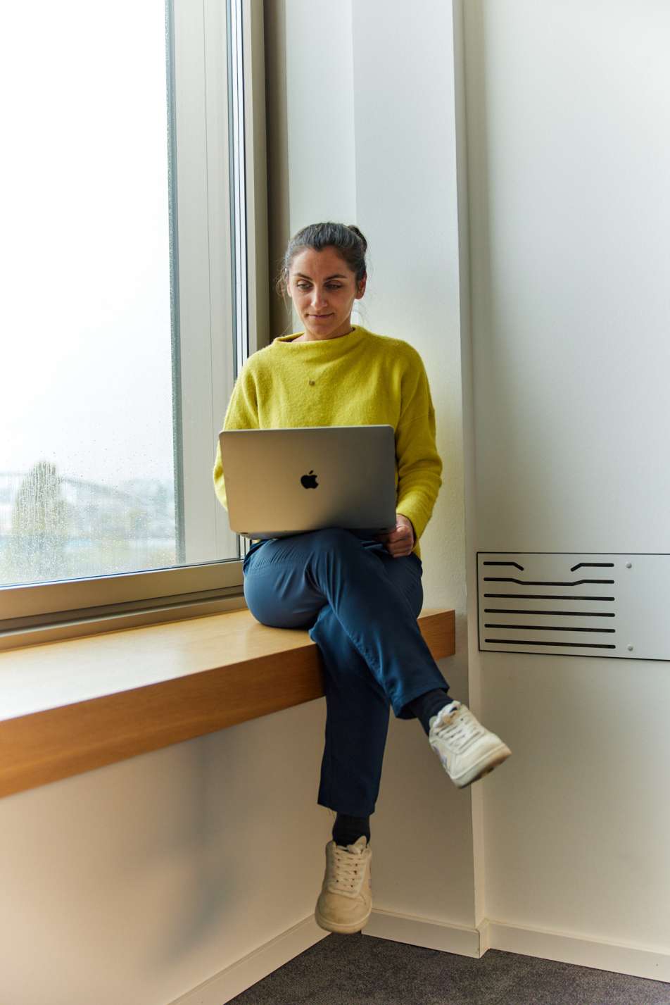 farbiges Foto von einer Frau mit einem Laptop, die auf einer Fensterbank sitzt