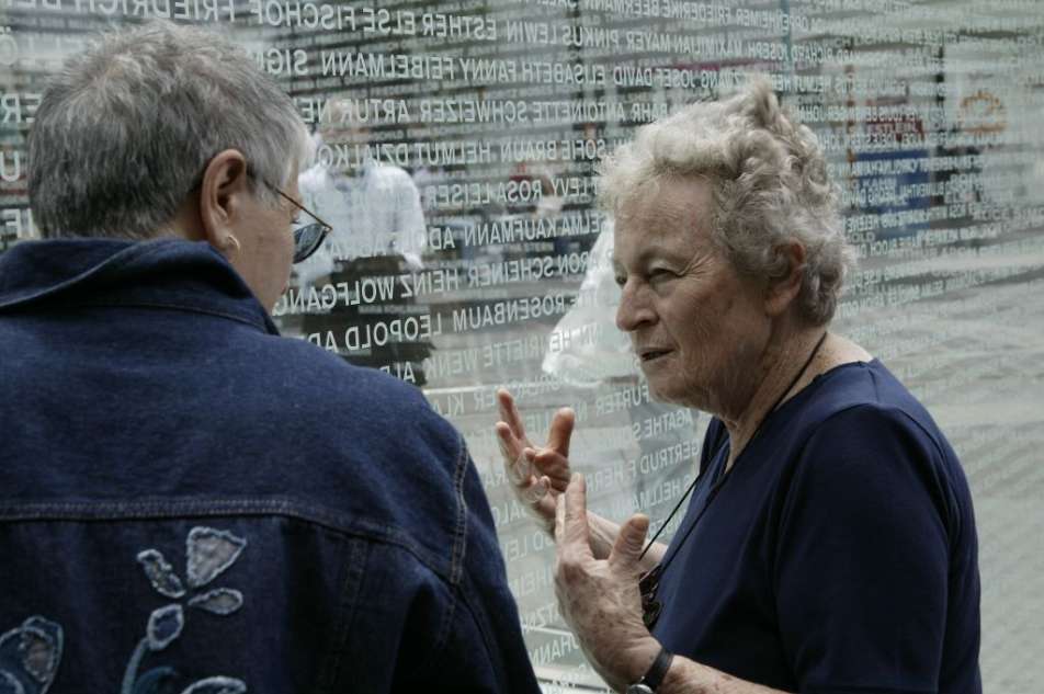 Farbiges Foto von zwei Frauen, die sich vor dem Denkmal für jüdische Opfer des Nationalsozialismus in Mannheim unterhalten